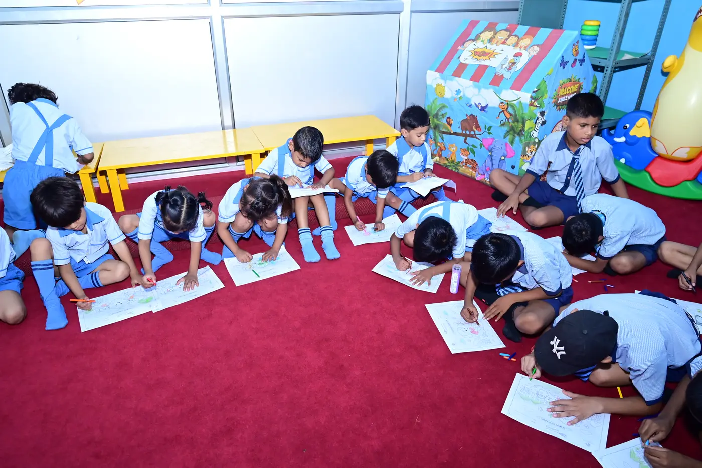 The activity room at Lords Public School, with low yellow benches, a play tent and soft toys, and children colouring on the floor.