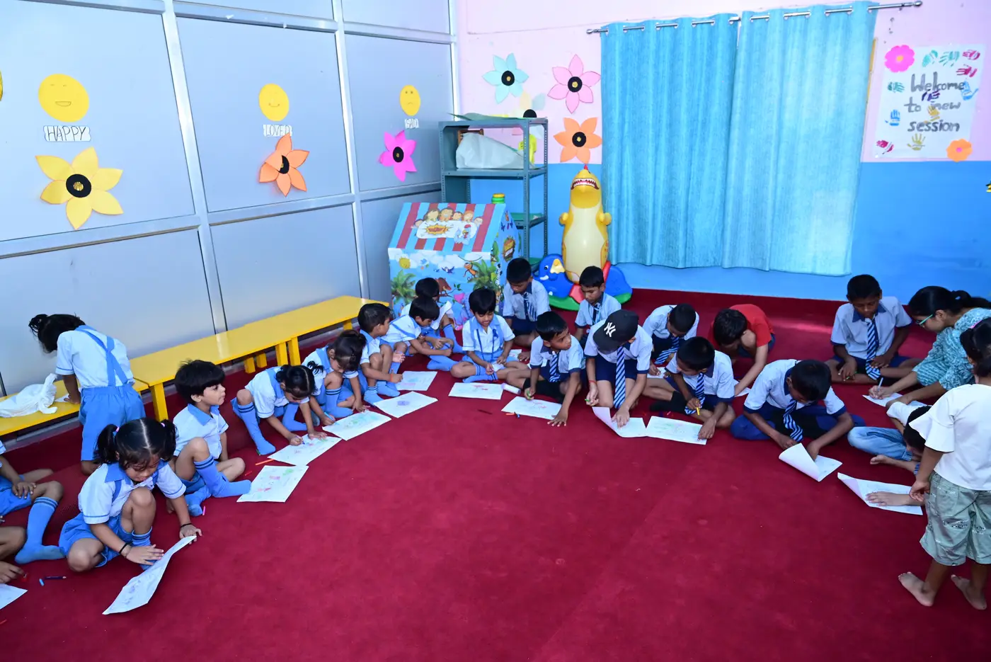 Children sitting on the floor of the activity room at Lords Public School, colouring competition sheets with pencils and crayons.