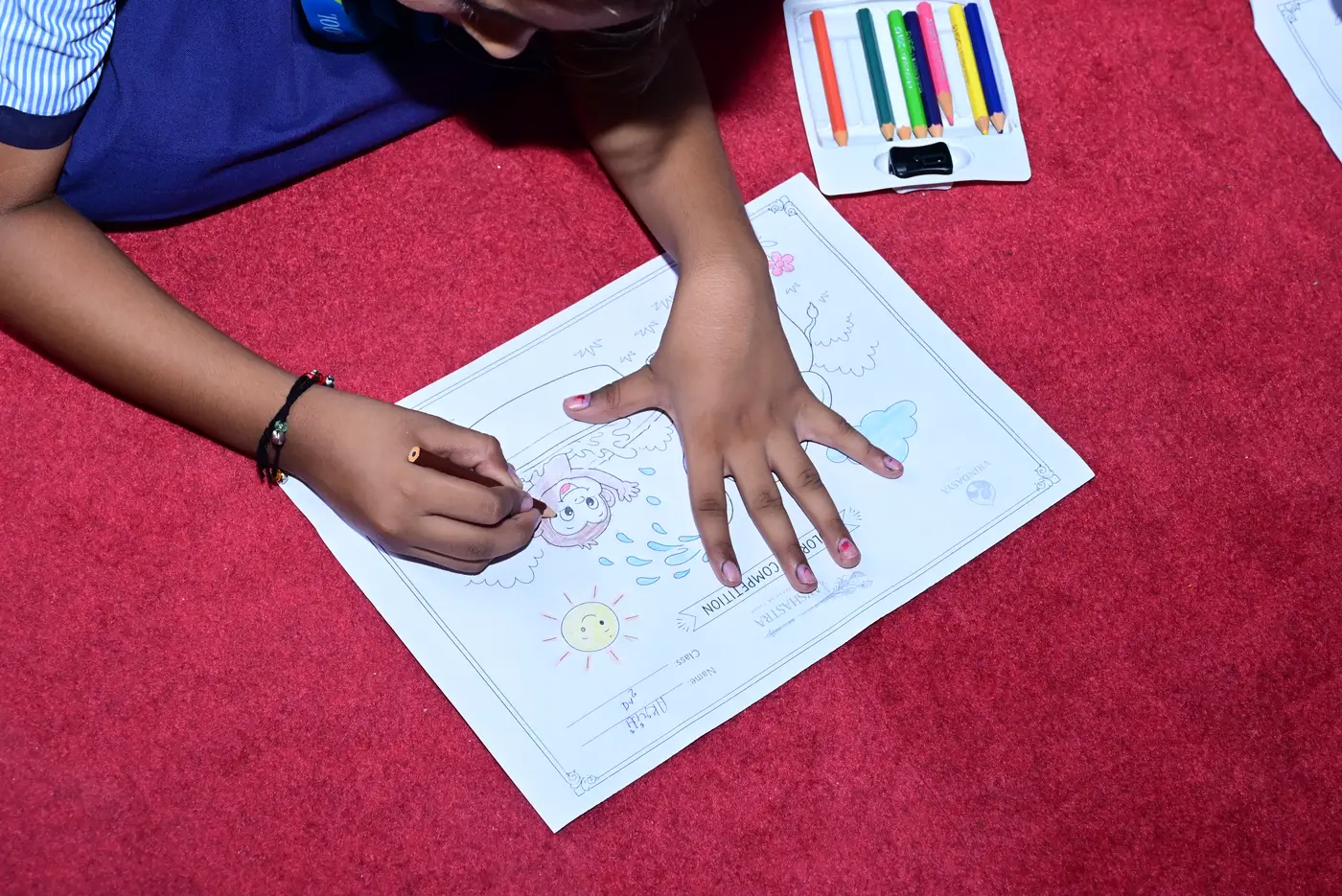 A close view of a child at Lords Public School colouring in a picture with a coloured pencil, a pencil case beside them.