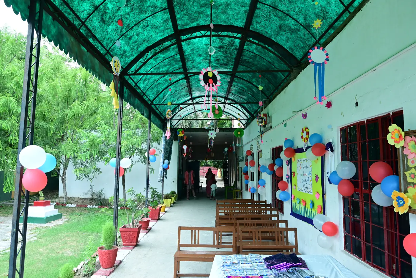 Under the green canopy at Lords Public School, with classroom doors decorated in coloured paper and balloons along the walkway.