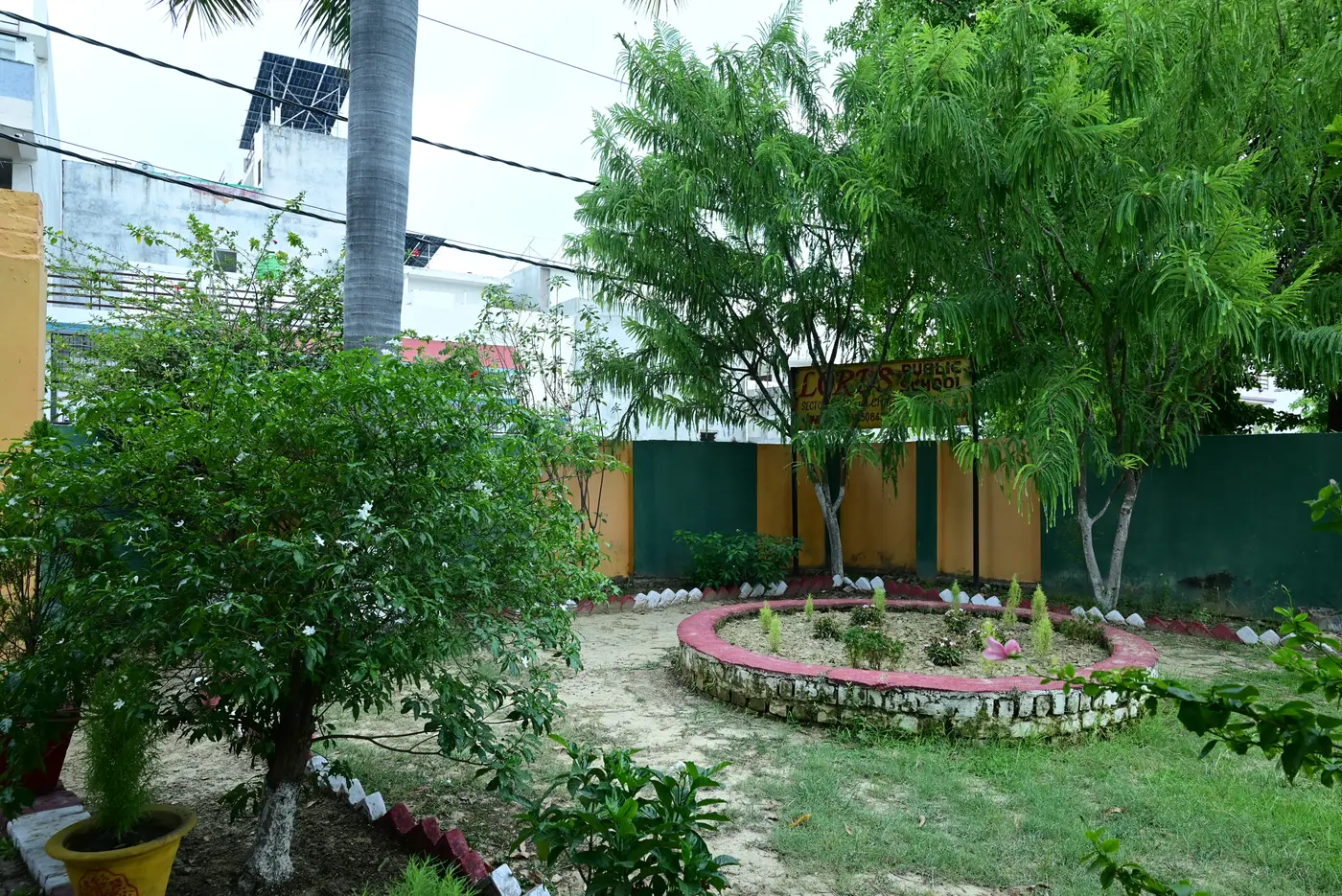The garden inside the Lords Public School campus, with a circular flower bed edged in brick and trees along the boundary wall.
