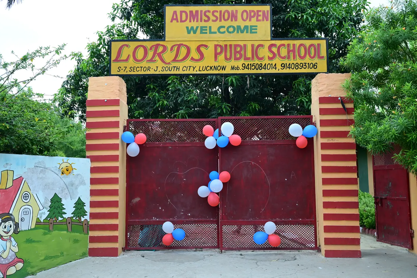 The red entry gate of Lords Public School, with the yellow signboard above it reading Admission Open, Welcome, Lords Public School.