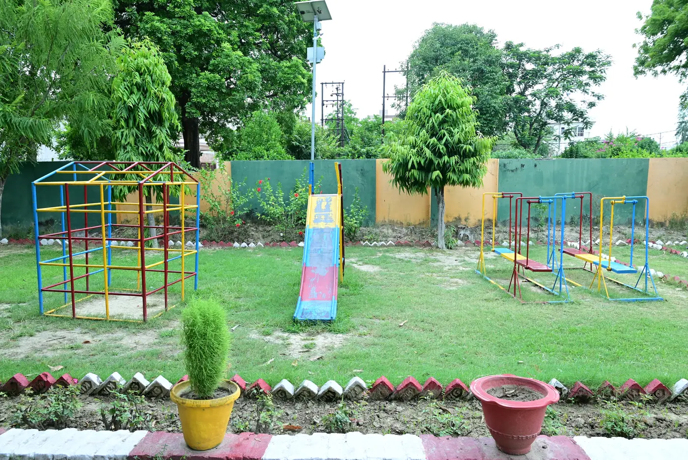 The playground at Lords Public School, with a climbing frame, a slide and see-saws on the grass.