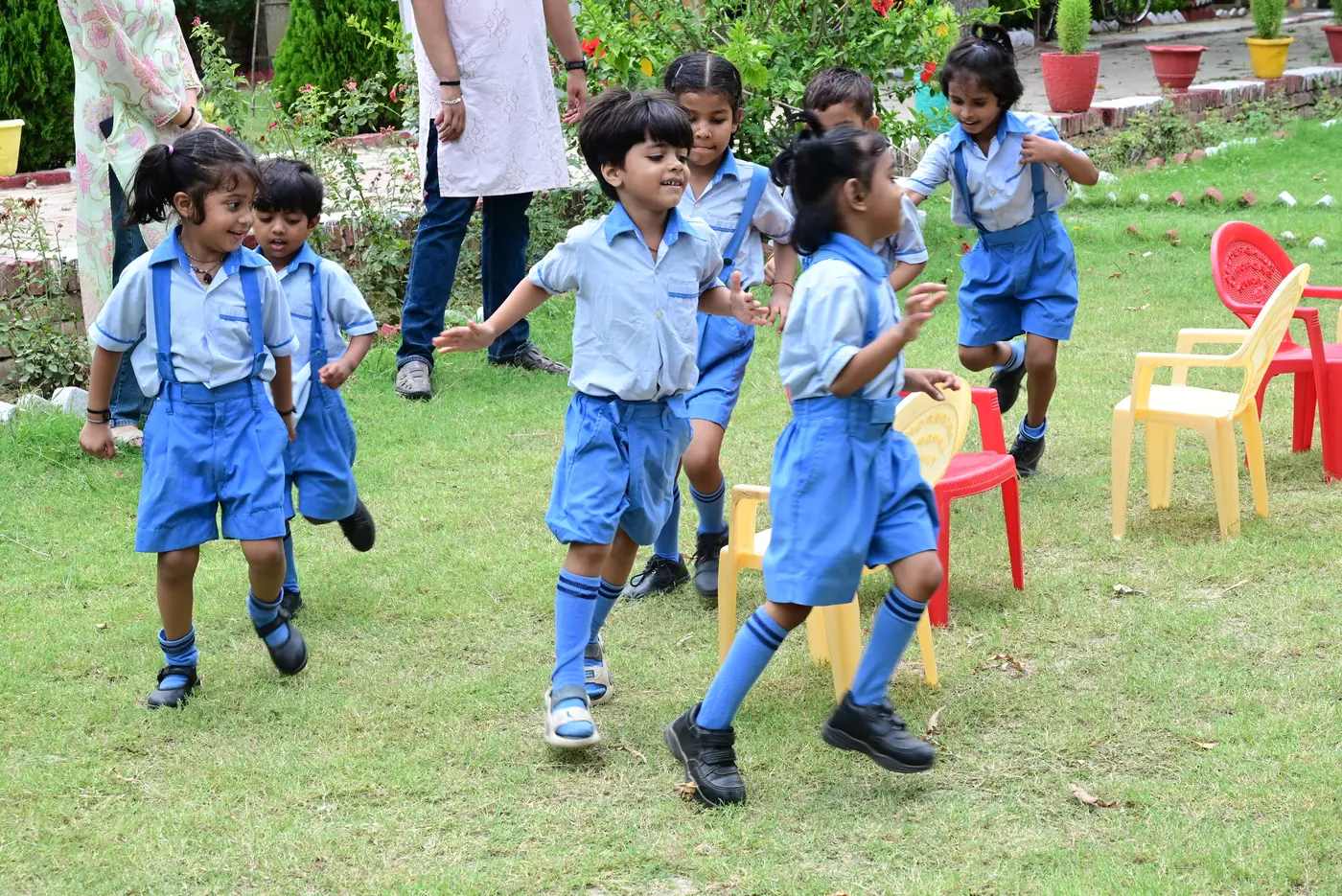 The youngest children at Lords Public School, in light blue uniforms, running around the chairs mid-game.